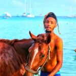 Island Hopping Man Stands In Sea Water With Horse